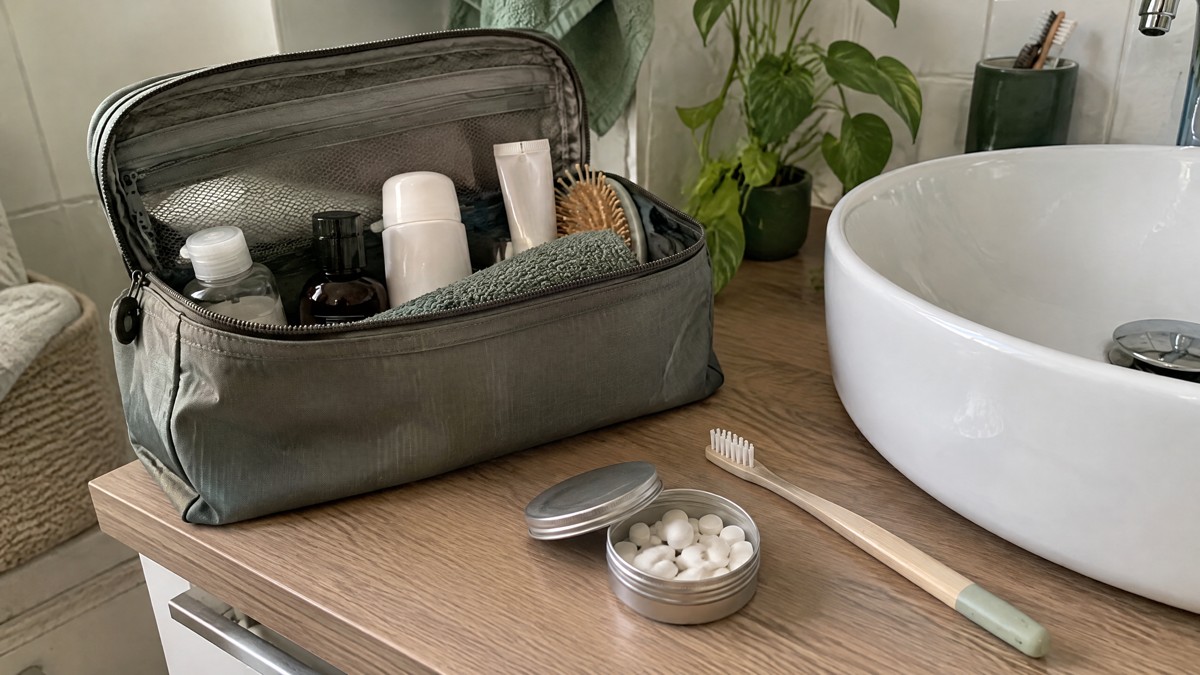 Mini tandpasta op reis: zijn tabletten handiger? A candid phone photo of an open travel toiletry bag on a bathroom counter, with a small unmarked aluminium tin holding t