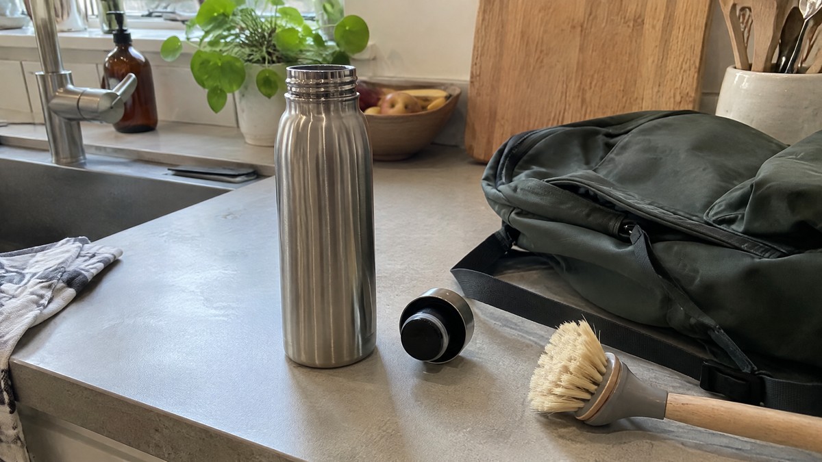 A candid phone photo of an open stainless steel water bottle and its cap lying underside-up on a kitchen counter beside