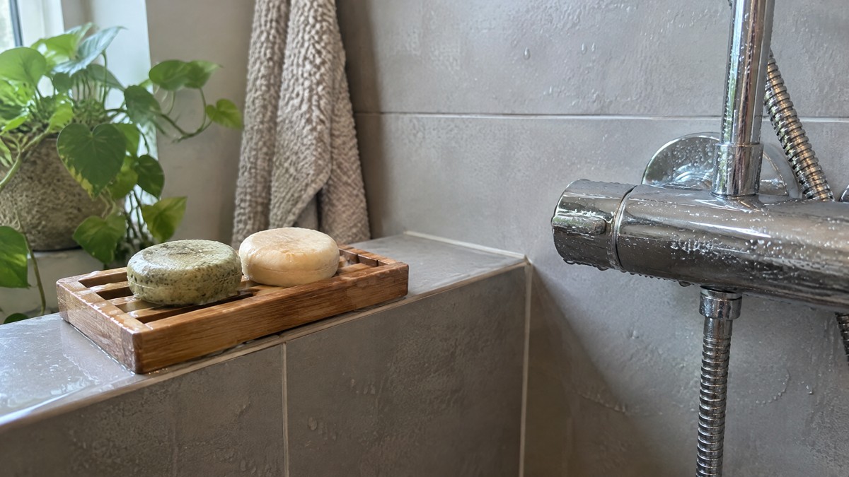 A candid phone photo of two slightly used solid hair-care bars on a draining soap dish beside a wet shower tap in an ord